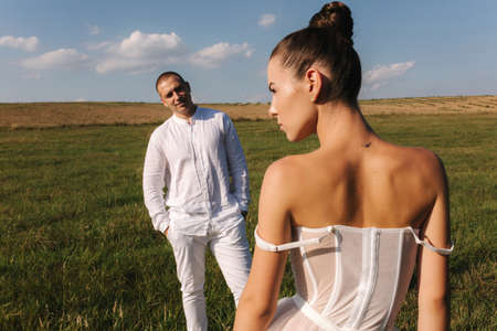 Gorgeous bride with handsome groom walkin in the field after wedding ceremony. Newlyweds posing to photographerの写真素材