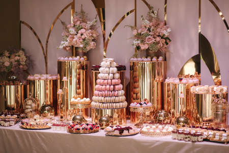 Luxury candy bar on golden wedding. Candy bar decorated by flowers standing of festive table with deserts, and cakes, strawberry tartlet, cupcakes and macarons. Wedding. Reception Tartlets