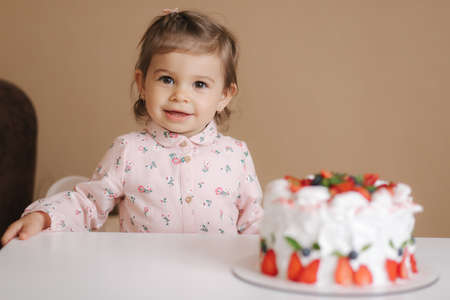 Cute little girl one and a hulf year old stand by delicious birthday cake. Eighteen month old girl verry happy and laughs. Vegetarian food. Lactose free and gluten free.の写真素材