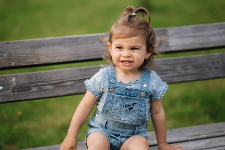 Adorable little girl laughing. Beautiful female kid in denim sitting on the bench in park. Happy...