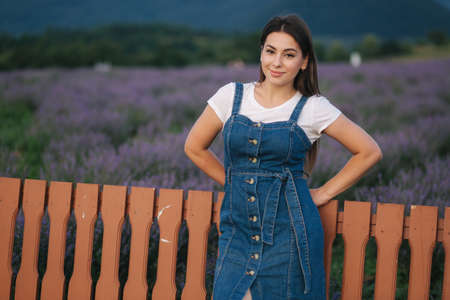 Attractive young woman walking in summer lavender field. Model dressed in denim sundressの写真素材