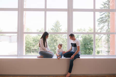 Little girl with mom and dad sits by the big window in studio. Family photosessionの写真素材