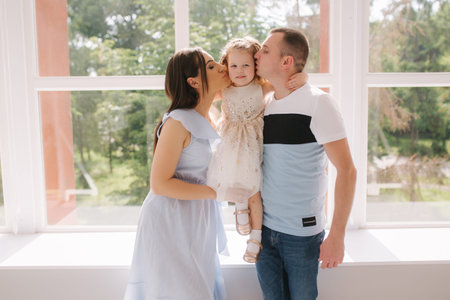 Family portrait of mom dand and little daughter in front of big window. Happy family. Mother and...