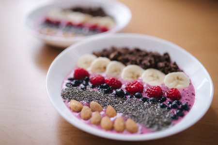 Smoothie bowl with fresh raspberry, blueberry, chia seeds, almonds, banana, and chocolate flakes. Morning breakfast on wooden table. Two ptales fith smoothie bows. Vegan foodの写真素材