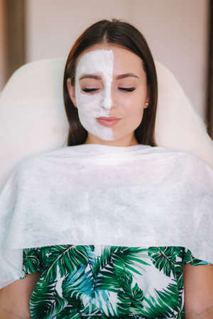 Beautiful woman with white mask on hulf of face. Attractive brunrtte woman in beauty salonの写真素材