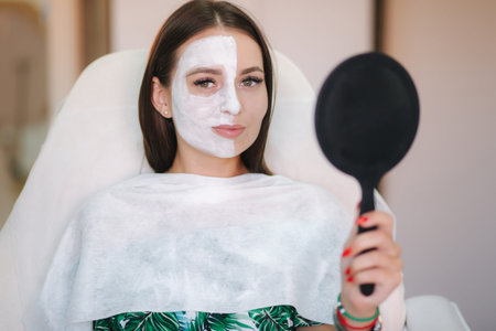 Beautiful woman with white mask on hulf of face. Attractive brunrtte woman in beauty salon