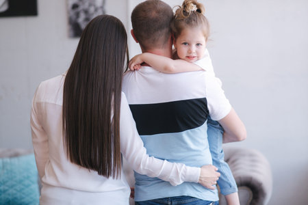 Back view of mom and dad hold daughter and kiss