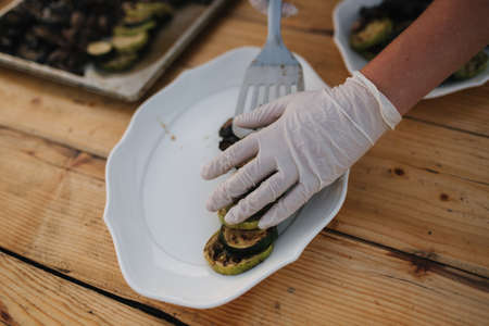 Waiter in white gloves put grilled vegetables on plate outdoorsの写真素材