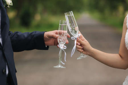 Groom and bride hold champagne glasses in the parkの写真素材