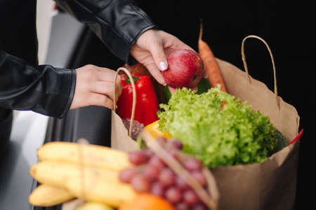 Close-up of groceries in eco package in car trunk. Hands of female packing vegetables and fruits after shipping in supermarketの写真素材