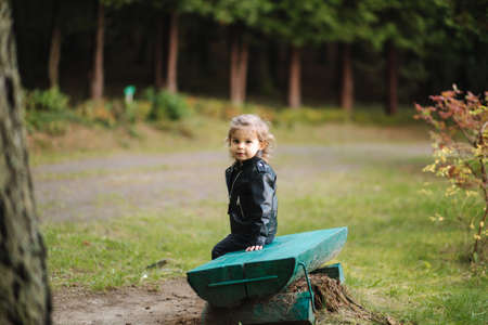 Cute little girl sitting on the bench in forest. Happy little kid walking outdoorsの写真素材