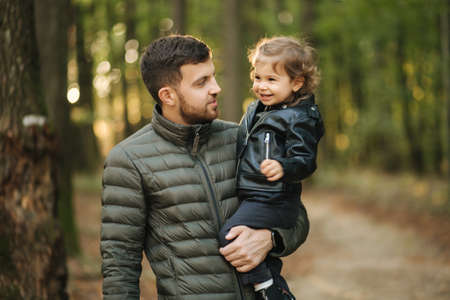 Portrait of beautiful little girl with her dad. Happy daughter on fathers hands in autumn forest. Two year girlの写真素材