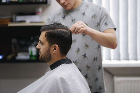 Handsome man getting haircut by barber while sitting in chair at barbershop.の写真素材
