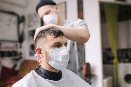 Man getting hair cut by scissor in barbershop. Barber use scissor and wearing mask during coronavirus pandemic. Professional barber work at home. Covid-19 quarantineの写真素材