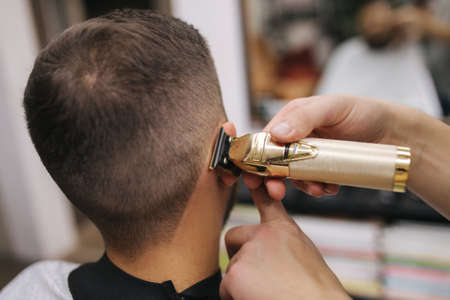 Professional hairdresser uses a hair clipper for fringing hair for a handsome bearder man. Barbershop. Closeupの写真素材