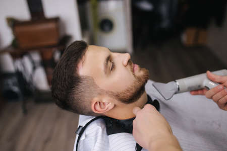 Professional hairdresser uses a hair clipper for fringing hair for a handsome bearder man. Barbershopの写真素材
