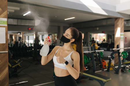 Brunettr woman with face mask cleaning exercise machine with disinfectant. Woman exercising in a gym during coronavirus epidemicの写真素材