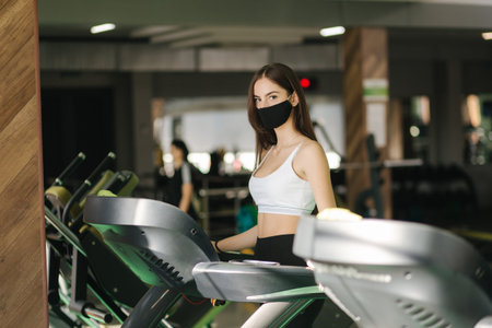 Female brunette jogging on running track in protective face mask in a gym during coronavirus...