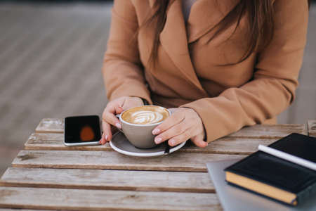 Close up of working proces in cafe outdoors. Woman writing down something in notebook. Cappuccino laptop and calendar on tableの写真素材