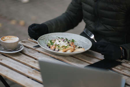 Close up of man in black gloves hold cutlery. Cafe concept during qurantine. Food outdoors in protective gloves. Fresh vegan salad with shrimpsの写真素材