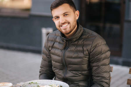 Handsome man sitting outdoors in cafe on terrace and smiled to cameraの写真素材