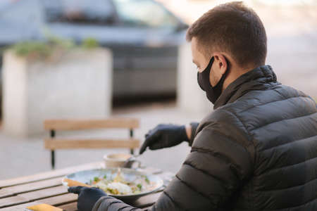 Man in black face mask sitting in cafe and prepared for eating vegan salad. Quarantine cafe concept. Covid-19の写真素材
