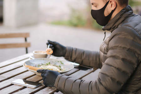Man in black face mask sitting in cafe and prepared for eating vegan salad. Quarantine cafe concept. Covid-19の写真素材