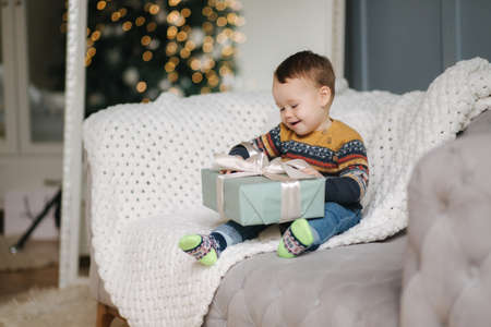 Little boy are sitting on coash with big present. Christmas mood at tomeの写真素材