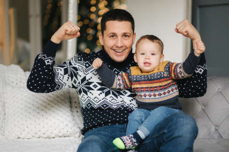 Portrait of dad and son sitting on a coach at home near the Christmas tree, all are smiling. Christmas family. Happinessの写真素材