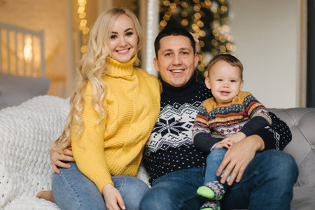 Portrait of dad, mom and son sitting on a coach at home near the Christmas tree, all are smiling....