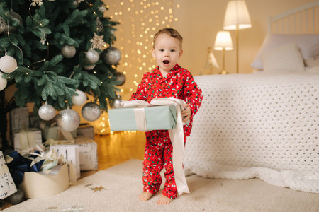 Cute little boy at home by the big Christmas tree looking for presents. Happy kid spend time on Holiday and enjoying every moment. Home aloneの写真素材