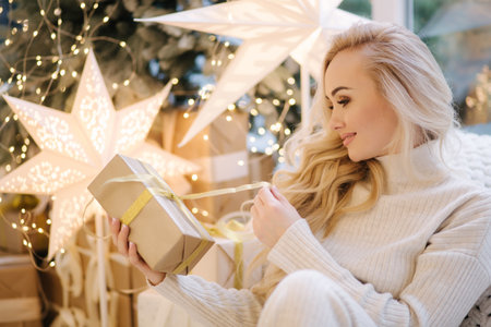 Portrait of Beautiful blond hair woman in pullover open present on Chrisrmas time. Elegant woman by Christmas tree. Attractive female hold present. Christmas moodの写真素材