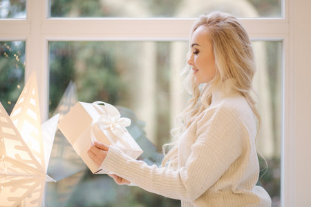 Portrait of Beautiful blond hair woman in pullover open present on Chrisrmas time. Elegant woman by Christmas tree. Attractive female hold present. Christmas moodの写真素材