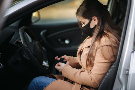 Beautiful young girl in a mask sitting in a car and put on protective gloves. Protective mask...