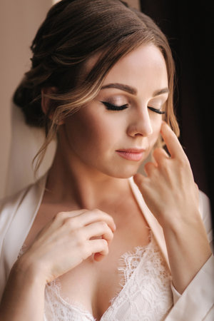 Portrait of attractive young bride in negligee. Beautiful woman stand by windowの写真素材