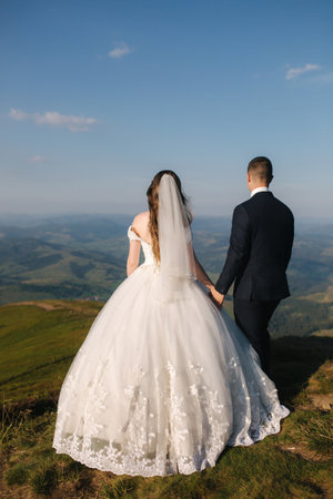 Wedding couple in mountains. Bride and groom standing on the hillの写真素材