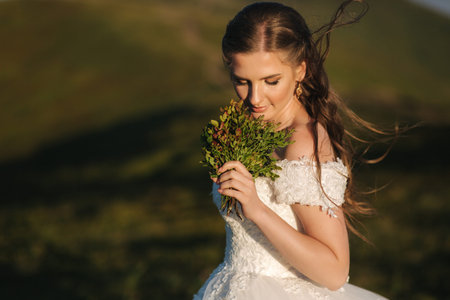 Beautiful young bride stand on the hill in mountais. Windy outdoor. Green hills on backgroundの写真素材