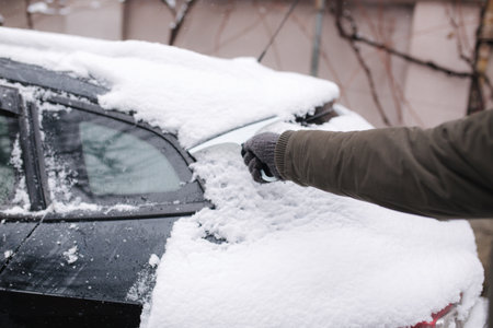 Close up of man is cleaning snowy window on a car with snow scraper. Focus on the scraper. Cold snowy and frosty morning. Black carの写真素材