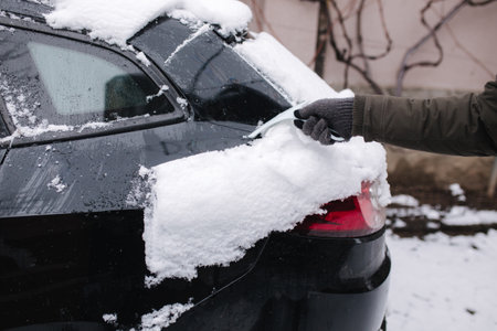 Close up of man is cleaning snowy window on a car with snow scraper. Focus on the scraper. Cold snowy and frosty morning. Black carの写真素材