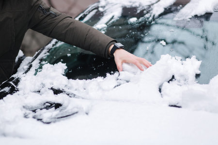 Handsome man clean his car from snow using hands. Winter outdoors