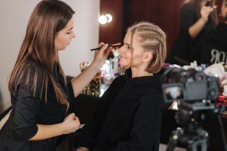 Side view of make up artist work with beautiful blond hair model in studio until camera films process of makeup. Blog of makeup artistの写真素材