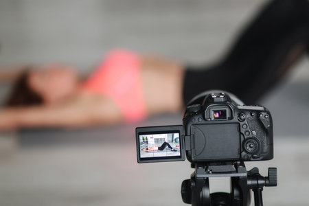 Attractive fitness woman blogger recording video on digital camera, training home in studio. Woman...