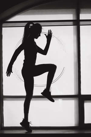 Silhouette of fit woman jump in front of big window in studio. Athletic woman have exercise in gymの写真素材