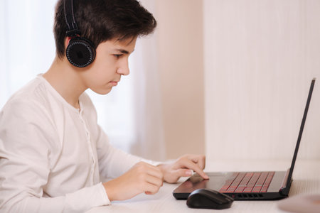 Teenage boy playing game on his pc computer in white room. Gamer capture video on web camera on laptopの写真素材