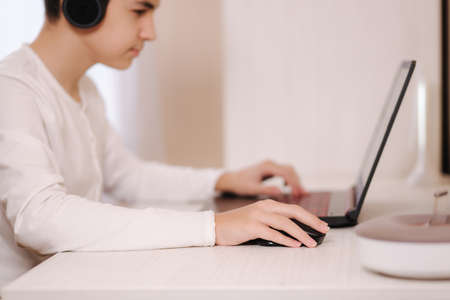 Teenage boy playing game on his pc computer in white room. Gamer capture video on web camera on laptop. Focus on handの写真素材