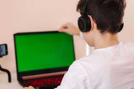 Young boy in headphones open laptop and start playing games. Handsome teenage boy steamerの写真素材
