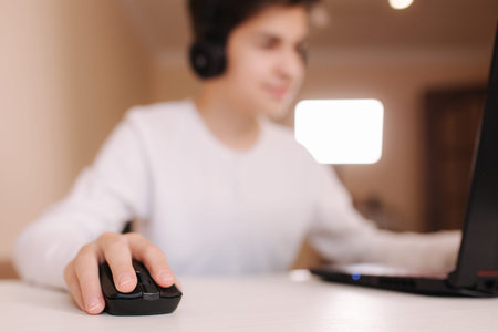 Teenage boy playing game on his pc computer in white room. Gamer capture video on web camera on laptop. Focus on handの写真素材