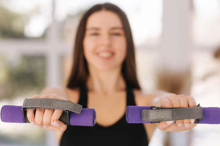 Attractive young woman training at home. Girl preparing for bikini season. Happy female use dumbbells for training. Focus on handsの写真素材