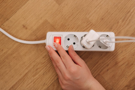 Top view of female hand turn on the extension cord at home. White cable connector