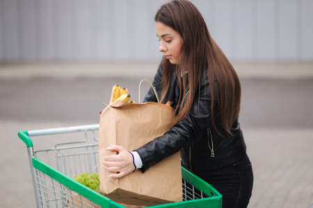 A process of young attractive woman taking groceries from a supermarket from the trolley to car truck. Food shopping during quarantine. Happy smiled womanの写真素材